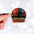 Load image into Gallery viewer, This image shows a hand holding the hide & seek sticker.