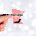 Load image into Gallery viewer, This image shows a hand holding the Minnesota with loon sticker.