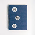 Load image into Gallery viewer, This image shows three Steampunk Sugar Skull labels on a notebook.