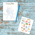 Load image into Gallery viewer, This image shows the notepad, a randomly chosen color (blue) pen, and paper sticker/label sheet that is available as part of the Watercolor Cruise Magnet Accessories.