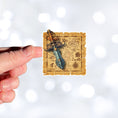 Load image into Gallery viewer, This image show a hand holding the Pirate Dagger on a Map Die-Cut Sticker.