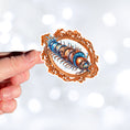 Load image into Gallery viewer, This image shows a hand holding the steampunk centipede sticker.