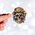 Load image into Gallery viewer, This image shows a hand holding the Steampunk Skull 5 Die-Cut Sticker.