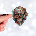 Load image into Gallery viewer, This image shows a hand holding the Steampunk Skull 6 Die-Cut Sticker.