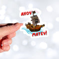 Load image into Gallery viewer, Hoist the main and prepare to board! This individual die-cut sticker is of a pirate ship under sail with the words "Ahoy Matey!" This image shows a hand holding the pirate ship sticker.