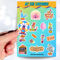 Load image into Gallery viewer, Who doesn't love going to the carnival? This sheet has stickers showing the big top, clowns, animals, and of course your favorite foods like hotdogs and cotton candy. This is an image of a hand holding one of the stickers above the sticker sheet.