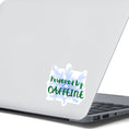 Load image into Gallery viewer, or those who like it, caffeine can be the magic elixir! This individual die-cut sticker has the words Powered by CAFFEINE in green over a background of blue electric/lightning bolts. This image shows the Powered by Caffeine sticker on the back of an open laptop.
