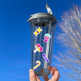 Load image into Gallery viewer, This sticker sheet is filled with stickers of all of your favorite sweet treats! Gumdrops, lollipops, cotton candy, and of course chocolate; this sheet will satisfy everyone's sweet cravings. This image shows a water bottle with stickers of wrapped hard candy, gumball machine, two lollipops, another wrapped hard candy, and a yellow candy cane applied to it.