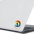 Load image into Gallery viewer, Hang 10 Bro! Catch a wave with this individual die-cut sticker featuring the silhouette of a female surfer inside the tube, all on a colored gradient background. Cowabunga! This image shows the Catching a Wave sticker on the back of an open laptop.