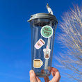 Load image into Gallery viewer, This sticker sheet has a dozen unique coffee related stickers to show how you feel about your favorite beverage. This image shows a water bottle with a sticker that says "Coffee Day" plus three stickers of different coffee drinks applied to it.