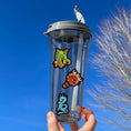 Load image into Gallery viewer, Set on a background of green scales, this sticker sheet has 16 different stickers of dragons and phoenix. This image shows a water bottle with three dragon stickers - a green dragon, a dragon mask, and a blue dragon - applied to it.