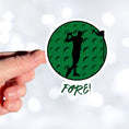 Load image into Gallery viewer, Show your love of golf with this individual die-cut sticker! This sticker shows the silhouette of a golfer about to swing, on a green golf ball background, with the word "Fore!" below. This image is of a hand holding the golf sticker.