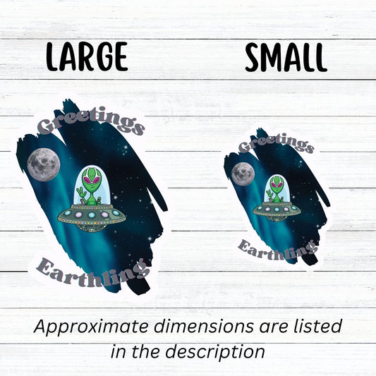 Welcome space aliens! This individual die-cut sticker features a friendly green space alien in a flying saucer, on a background of stars with the moon behind, and the words "Greetings Earthling". This image shows the large and small flying saucer stickers next to each other.