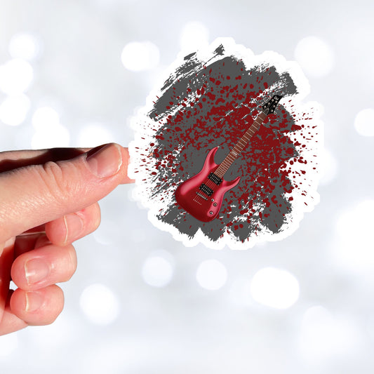 This guitar sticker is great for any guitarist, whether a beginner or a seasoned shredder! This individual die-cut sticker features a burgundy electric guitar on a gray and burgundy paint splattered background. Turn it up! This image shows a hand holding the guitar sticker.