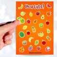 Load image into Gallery viewer, Filled with sticker images of cute fruit, this sticker sheet is sure to put a smile on anyone's face! This image shows a hand holding a sticker of a smiling pear over the sticker sheet.