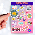 Load image into Gallery viewer, Feel good with these inspirational thoughts as stickers! This sheet has a dozen stickers with inspirational sayings, plus some smaller stickers to help brighten anyone's day. This image shows a hand holding a happy face sticker with the caption "Happy Thoughts" over the sticker sheet.