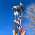 Load image into Gallery viewer, Celebrate summer, and the 4th of July in the USA. This sticker sheet has all of your favorite summer time foods like BBQing, burgers, hot dogs, and corn on the cob. Plus fireworks and red, white, and blue images. This image shows a water bottle with four summer time and patriotic stickers applied to it.