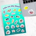 Load image into Gallery viewer, Teaming with sea life, this sticker sheet is filled with sticker images of fish, sea turtles, and coral! Take the reef with you anywhere with these beautiful stickers. This image shows the sticker sheet next to an open laptop with stickers of a yellow angle fish and coral reef applied below the keyboard.