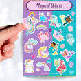 Load image into Gallery viewer, Mermaids, rainbows, and unicorns; it's our Magical World sparkle sticker sheet! This sticker sheet is filled with fun and cute magical images, and it has a sparkle overlay so it glitters in the light! This image is of a hand holding a unicorn sticker above the sticker sheet.