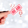 Load image into Gallery viewer, Music, TV, Podcast, or even Amateur Radio - this sticker is great for anyone who is On Air! This individual die-cut sticker is in neon red with the words On Air above a microphone with music notes above. Please note that the large version of this sticker is on a white background and cut around the image, and the small version is on a black circle. This image shows a hand holding the large On Air sticker.
