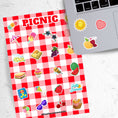 Load image into Gallery viewer, Pack the picnic basket and grab a blanket; we're going on a picnic! This sticker sheet has sticker images of all your favorite picnic foods and activities like sandwiches, fruit, ice cream, and lemonade all on a red and white checked tablecloth background. This image shows the sticker sheet next to an open laptop with stickers of the sun, a red and white checked heart, and an ant holding a yellow apple, applied below the keyboard.
