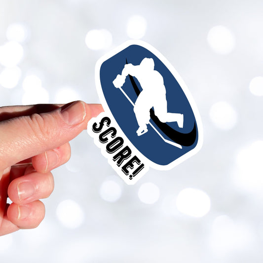 Grab your stick, lace up your skates, and head to the rink! This individual die-cut sticker features a hockey player silhouette on a blue hockey puck with the word "Score!" on the lower left side. This image shows a hand holding the hockey sticker.