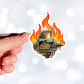 Load image into Gallery viewer, This individual die-cut steampunk sticker features a brown engine with a cutaway to show the gears inside, on a background of yellow, orange, and red flames. This image shows the steampunk engine sticker being held above a white background.