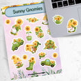 Load image into Gallery viewer, Sunflowers and Gnomes; what a perfect combination! This sticker is filled with stickers of sunflowers and gnomes with sunflowers. This image shows the sticker sheet next to an open laptop with a watering can filled with sunflowers sticker and a gnome holding a large sunflower sticker applied below the keyboard.