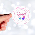 Load image into Gallery viewer, Sweet as Ice Cream! This round individual die-cut sticker has the word Sweet with two ice cream bars in the center surrounded by pink and purple circular dots. This makes a great gift for your sweetie! This image shows a hand holding the Sweet - Ice Cream sticker.