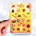 Load image into Gallery viewer, This festive Thanksgiving sticker sheet is perfect for decorating or scrapbooking. It features all of your favorite Thanksgiving images and inspirational sayings. Let the feast begin! This image shows a hand holding a basket of pies over the Happy Thanksgiving sticker sheet.