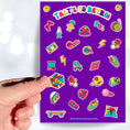 Load image into Gallery viewer, This sticker sheet is filled with images of items from the 70's, 80's, and 90's. Sticker images include a troll doll, roller skate, Rubik's cube, and a skateboard. This image shows a hand holding a Rubik's cube above the sticker sheet.