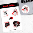 Load image into Gallery viewer, Trash Polka uses red, black, and white with a combination of abstract, surrealistic, and realistic images. This sticker sheet has four larger stickers from our die-cut sticker collection combined with a smaller sticker of a raven flying across a red sun. The stickers are the Trash Polka Woman's face, Trash Polka Clock, Trash Polka Owl, and Trash Polka Sugar Skull Woman. This image shows the sticker sheet next to an open laptop with the Trash Polka Clock sticker applied below the keyboard.