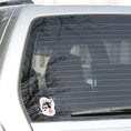 Load image into Gallery viewer, Trash Polka uses red, black, and white with a combination of abstract, surrealistic, and realistic images, and this individual die-cut sticker features a woman wearing sunglasses with her hair tied up on a white background with red swirls. This image shows the trash polka woman sticker on the back window of a car.