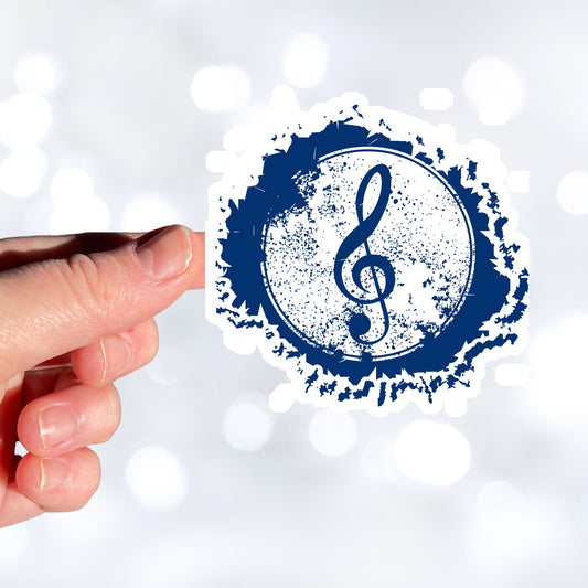 This individual die-cut sticker features a blue treble clef with a paint splattered background. Perfect for performers and music lovers alike! This image shows a hand holding the treble clef sticker.