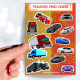 Load image into Gallery viewer, This sticker sheet has a collection of truck and car stickers; perfect for kids and adults who like their four wheel friends! This sheet has five different truck stickers and seven different car stickers on an orange and yellow background. This image shows a hand holding a sticker of a semi truck above the sticker sheet.