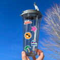 Load image into Gallery viewer, Pack your sunscreen and flip flops for a Vacation in the Sun! This sticker sheet is filled with summer vacation sticker images like the sun with sunglasses, a rubber ducky float ring, ice cream, and a sailboat. This image shows a water bottle with stickers of a car carrying a surfboard, a pink starfish, the sun with sunglasses, a sailboat, and a palm tree, applied to it.