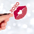 Load image into Gallery viewer, This individual die-cut sticker pretty much speaks for itself! It features a pair of lips with XOXO written above. Nuff said! This image shows a hand holding the XOXO sticker.