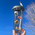 Load image into Gallery viewer, This sticker sheet has a sparkle overlay with 19 different stickers of cute ladybugs and bees. This image has a water bottle with stickers of a smiling bee, "Love" written in ladybugs, a black and yellow bee heart, and 2 ladybugs in the flowers applied to it.