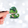 Load image into Gallery viewer, This image shows a hand holding the crocodile wearing a hat sticker.
