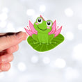 Load image into Gallery viewer, This image shows a hand holding the froggy on a lily pad sticker.
