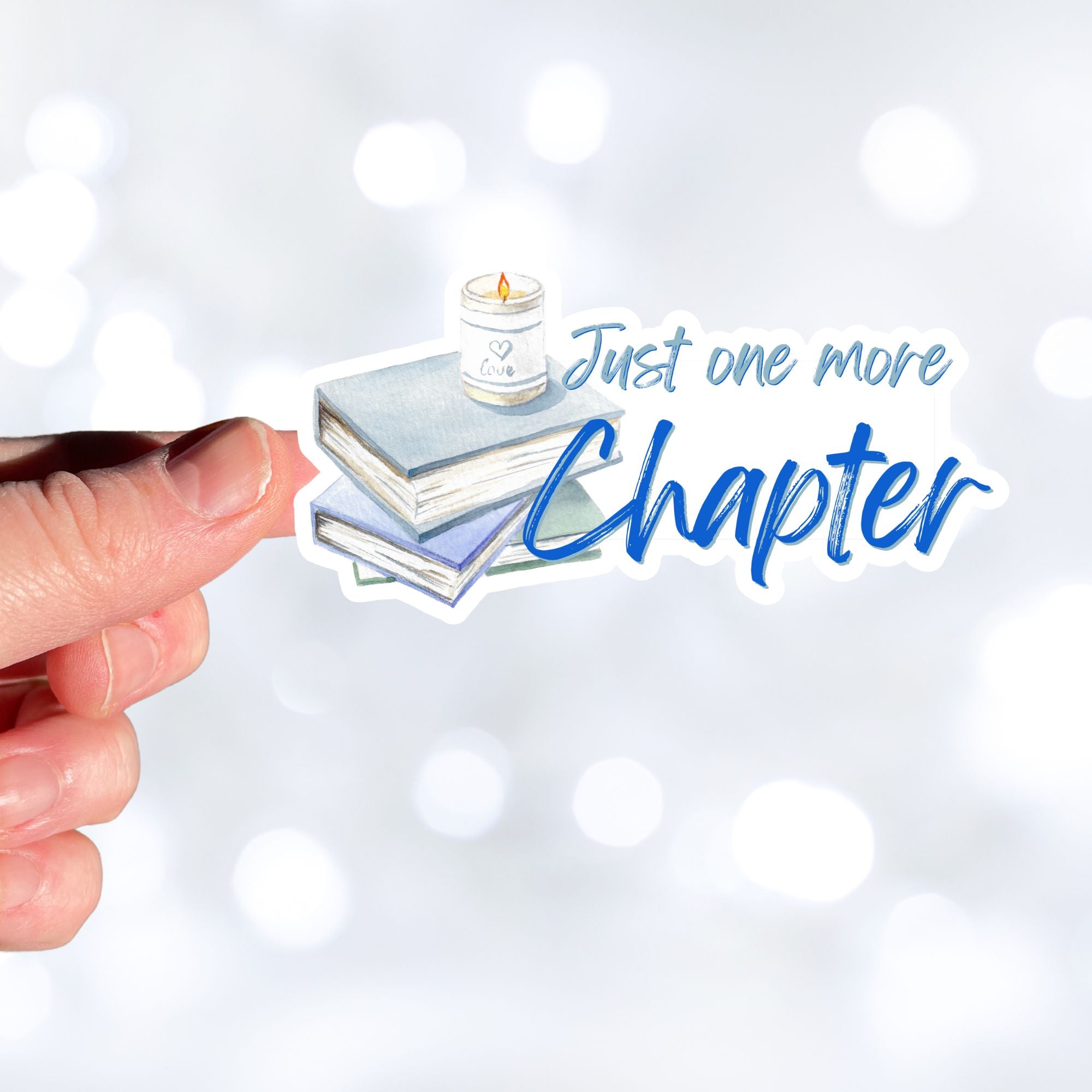 Love to read? If so then you know that there's always time for one more chapter! This individual die-cut sticker features a stack of books with a candle on top, and the words "One More Chapter", all in blue and gray on white. Enjoy your reading! This image shows a hand holding the Just One More Chapter sticker.