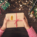 Load image into Gallery viewer, This image shows the holiday sticker on a package being held by elf hands.
