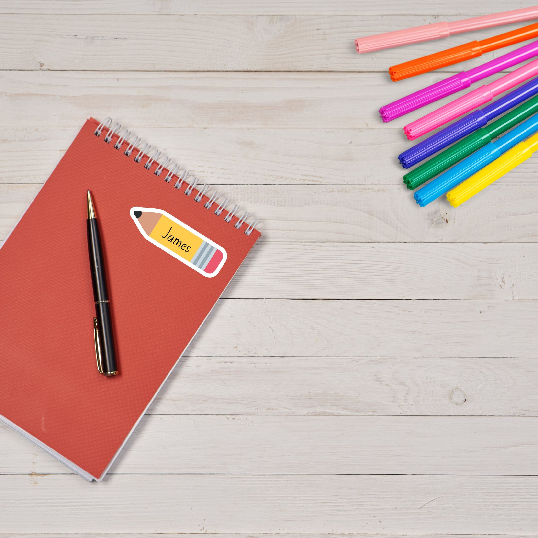 This image shows the personalized school sticker on a notebook with colored pens in the upper right corner..