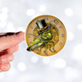 Load image into Gallery viewer, This image shows a hand holding the steampunk grasshopper sticker.
