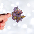 Load image into Gallery viewer, This image shows a hand holding the steampunk rose sticker.
