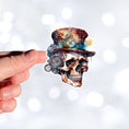 Load image into Gallery viewer, This image shows a hand holding the Steampunk Skull 3 Die-Cut Sticker.
