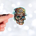 Load image into Gallery viewer, This image shows a hand holding the Steampunk Skull 4 Die-Cut Sticker.
