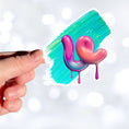 Load image into Gallery viewer, This individual die-cut sticker is one you either like or don't like; it's very unique! Featuring a 3D paint drip in pinks and purples over a green and blue paint swath, this sticker is hard to explain but pretty interesting to see. This image shows a hand holding the 3D Drip die-cut sticker.
