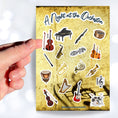 Load image into Gallery viewer, This sticker sheet celebrates all things music! Strings, brass, woodwinds, and percussion stickers that are perfect for any music lover. This image shows a hand holding a violin above the sticker sheet.
