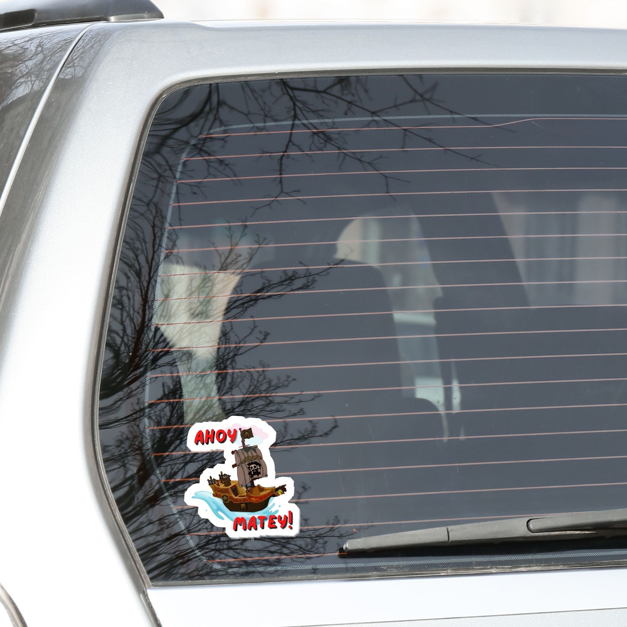 Hoist the main and prepare to board! This individual die-cut sticker is of a pirate ship under sail with the words "Ahoy Matey!" This image shows the pirate sticker on the back window of a car.